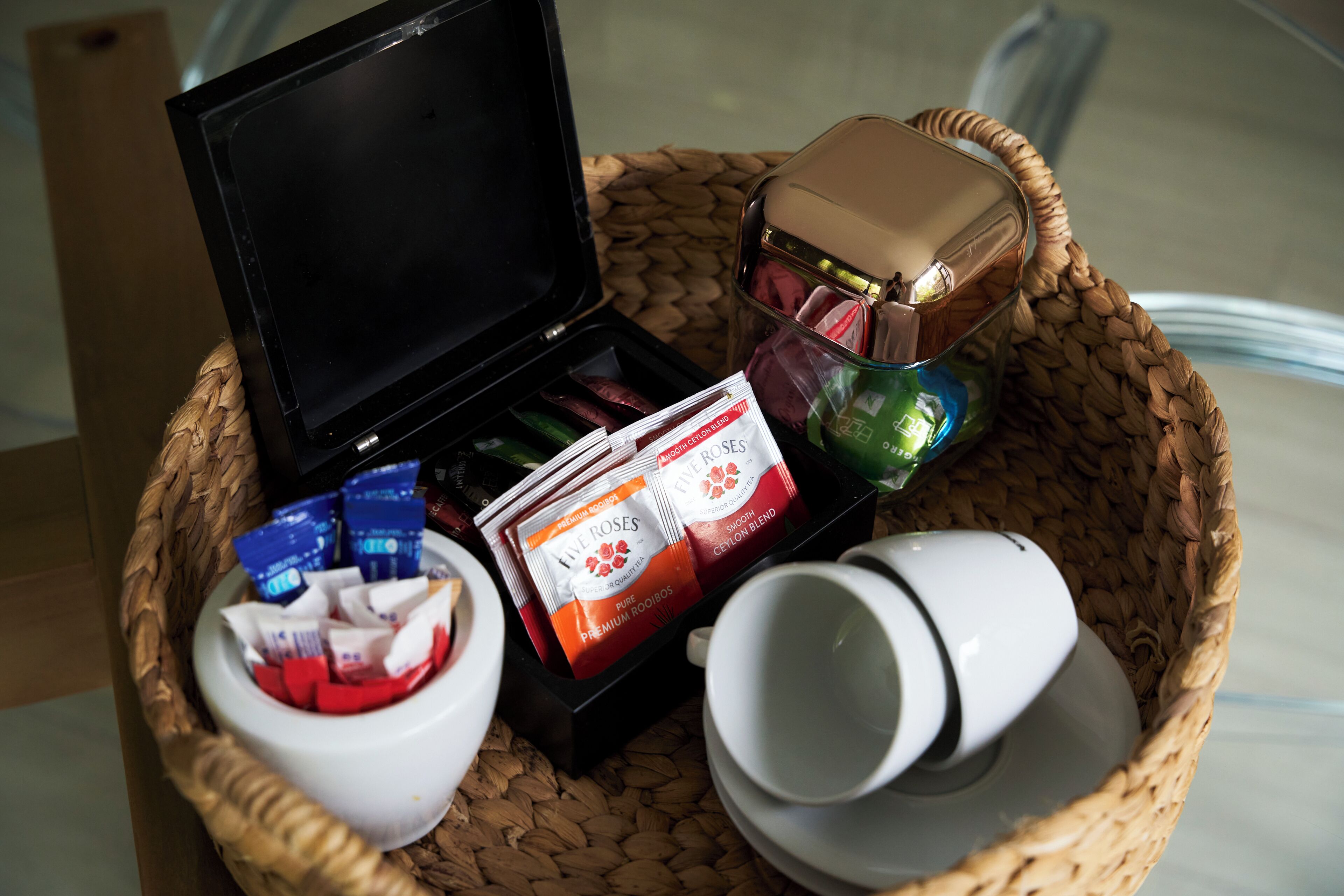Un panier tressé contenant une machine à café, une tasse et des sachets de thé.