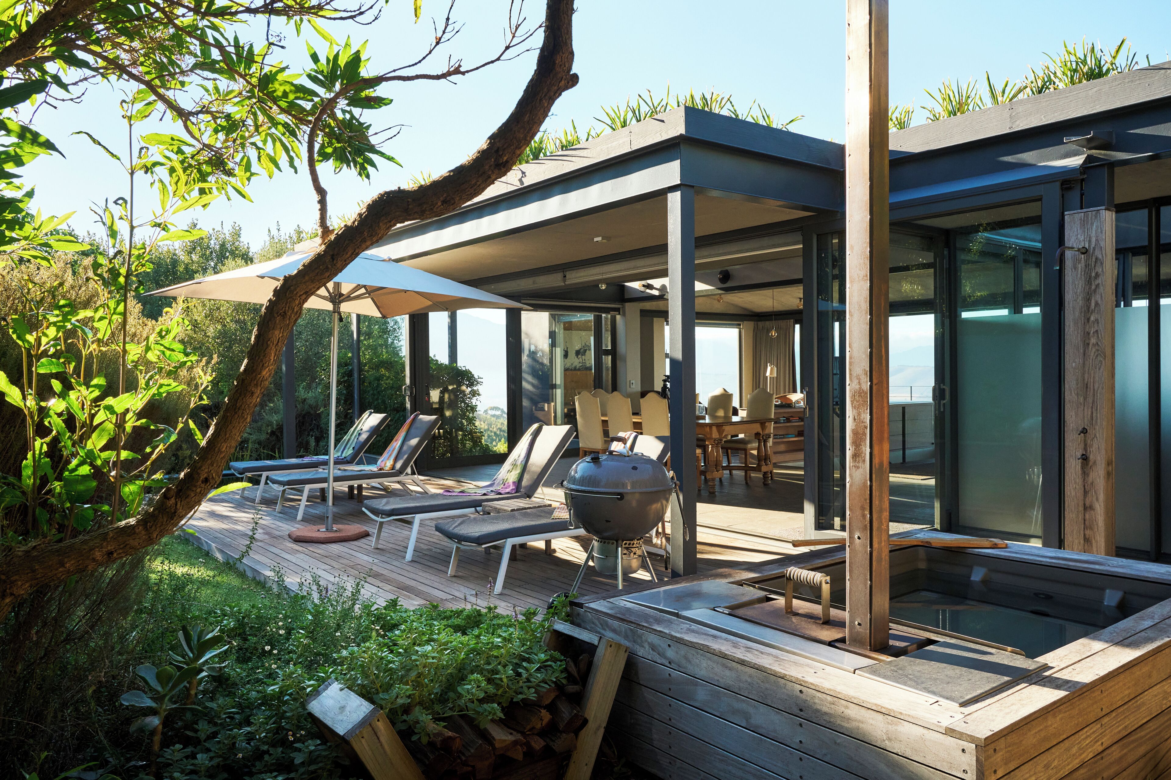 A modern outdoor deck with lounge chairs, a barbecue grill, and a hot tub.