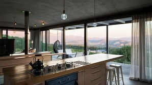 A modern kitchen with a large island, large windows, and a view of the mountains. - Spanish Farm Boutique Hotel & Villas (Cape Town)