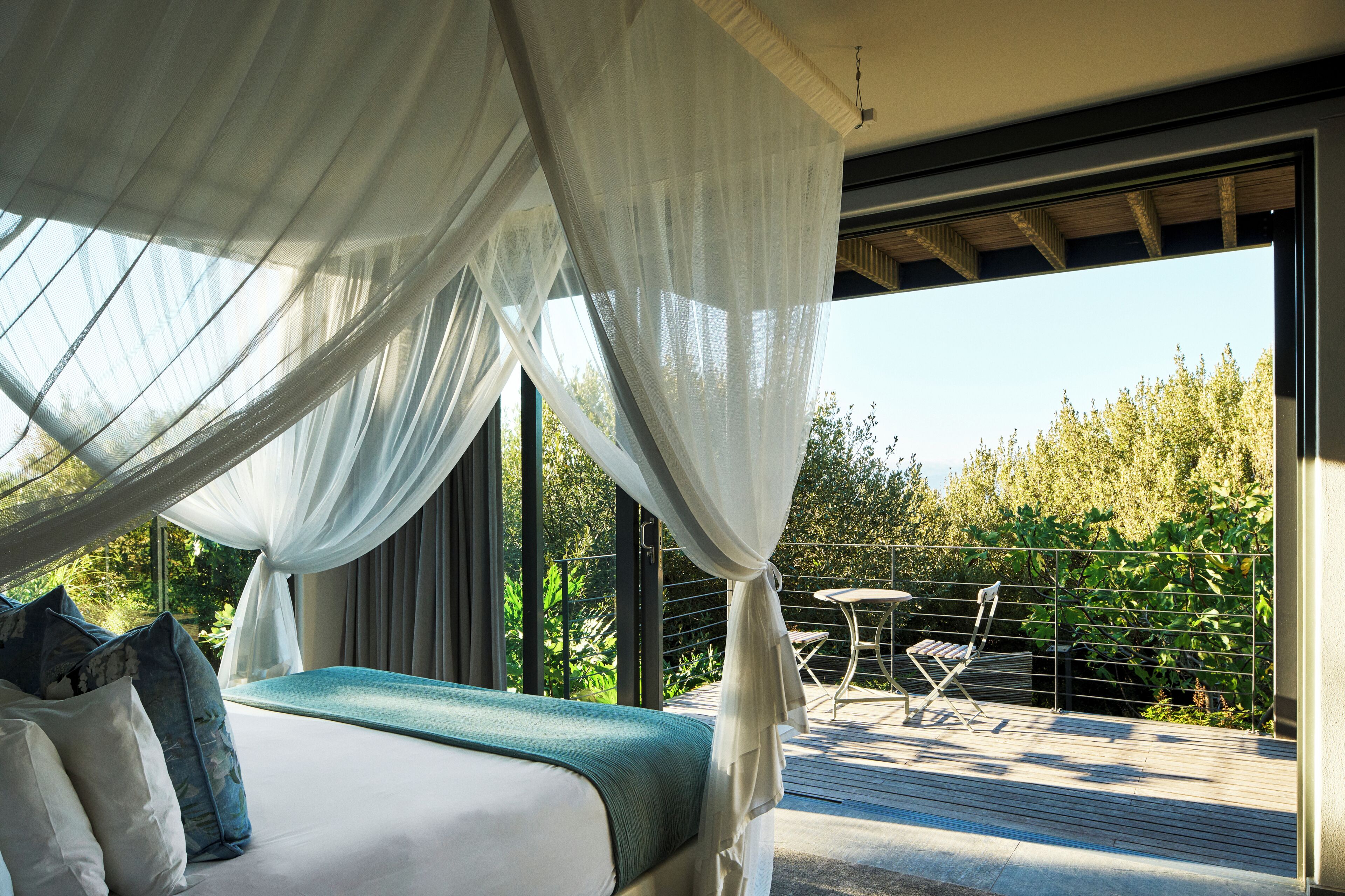 A bedroom with a bed, a canopy, and a view of a balcony with a table and chairs.