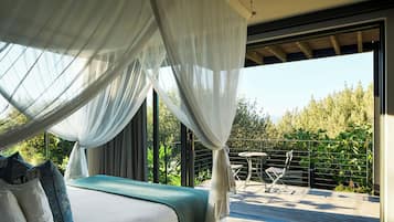 A bedroom with a bed, a canopy, and a view of a balcony with a table and chairs.