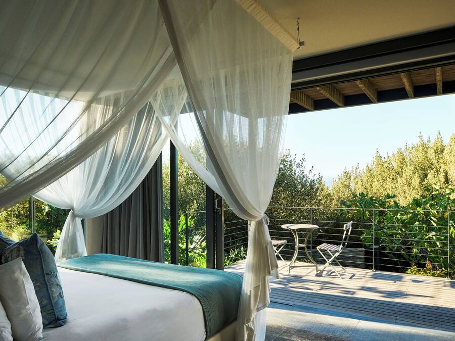 A bedroom with a bed, a canopy, and a view of a balcony with a table and chairs.