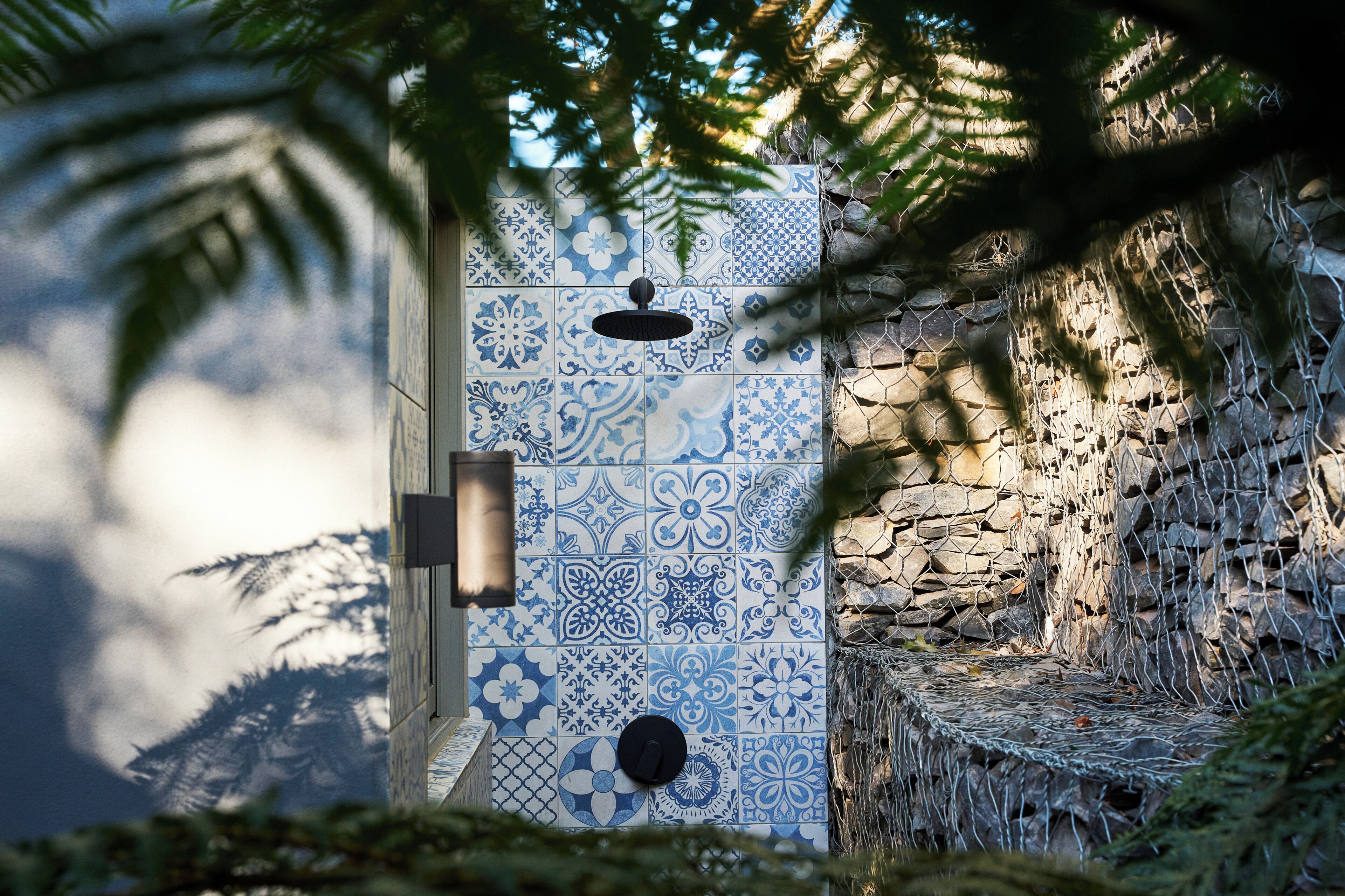 Paredes revestidas de azulejos com padrão geométrico, uma porta com puxador redondo e uma parede de pedra com tela de arame.