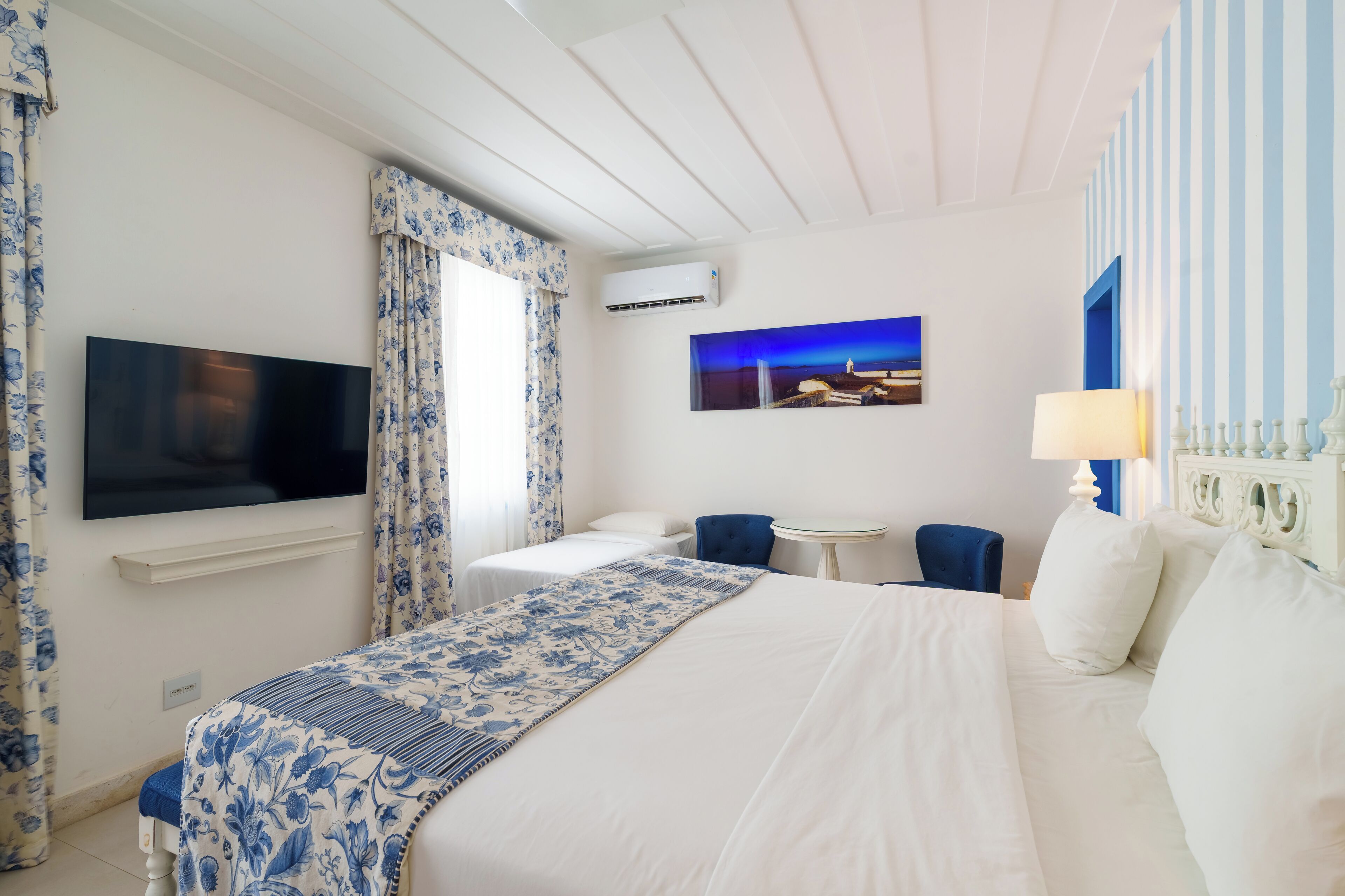 A hotel room with a large bed, a TV mounted on the wall, a small table, and a chair.