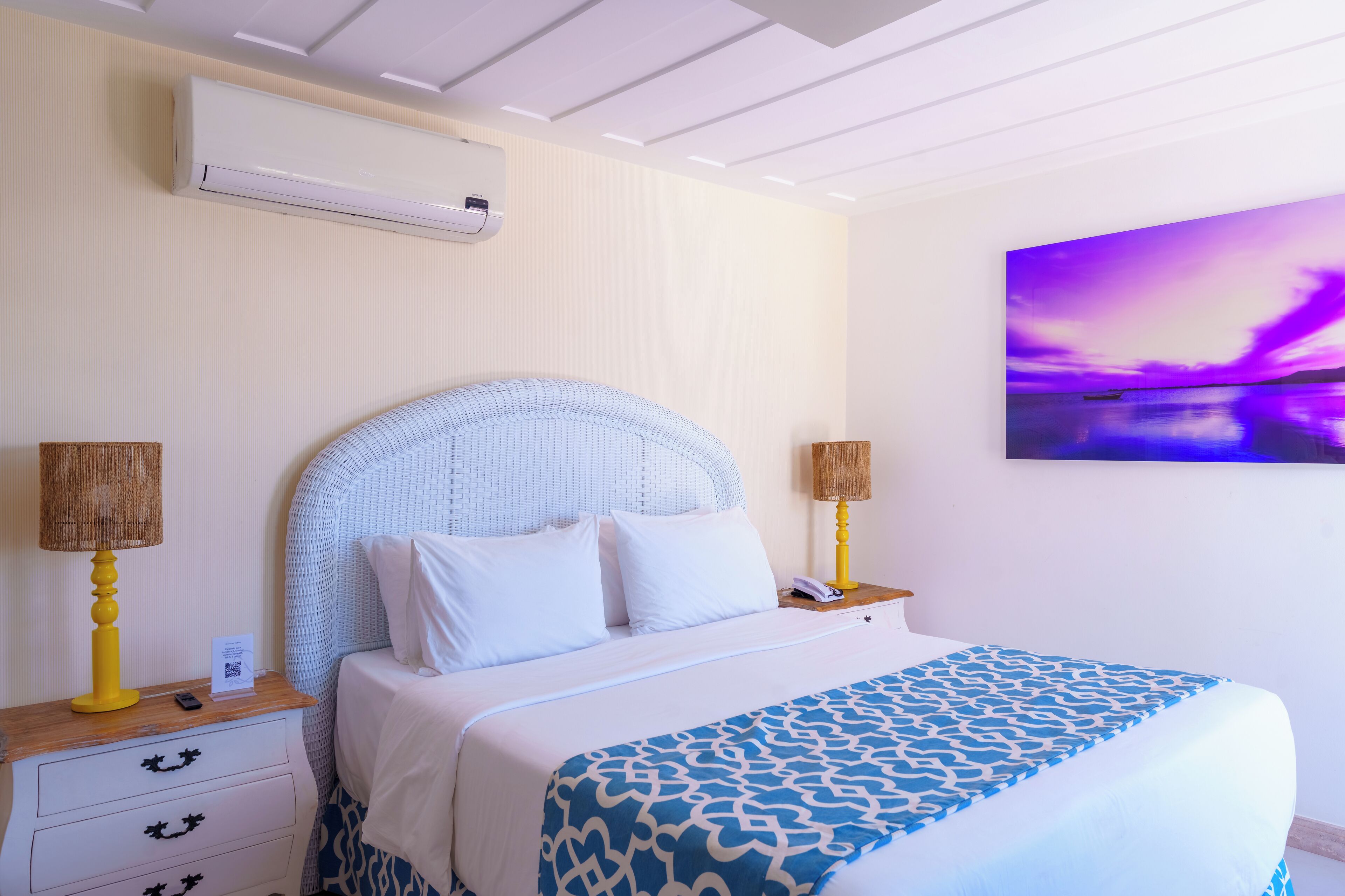 Ein Schlafzimmer mit einem Bett, Nachttischen, einer Wand-Klimaanlage und einem Sonnenuntergangsbild.