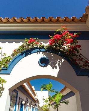 An arched entrance with a blue and white facade, red flowers, and a clear blue sky. - Hotel Solar do Arco (Cabo Frio)