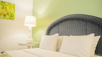 A neatly made bed with white linens and pillows, a white bedside table with a lamp, and a wicker headboard.