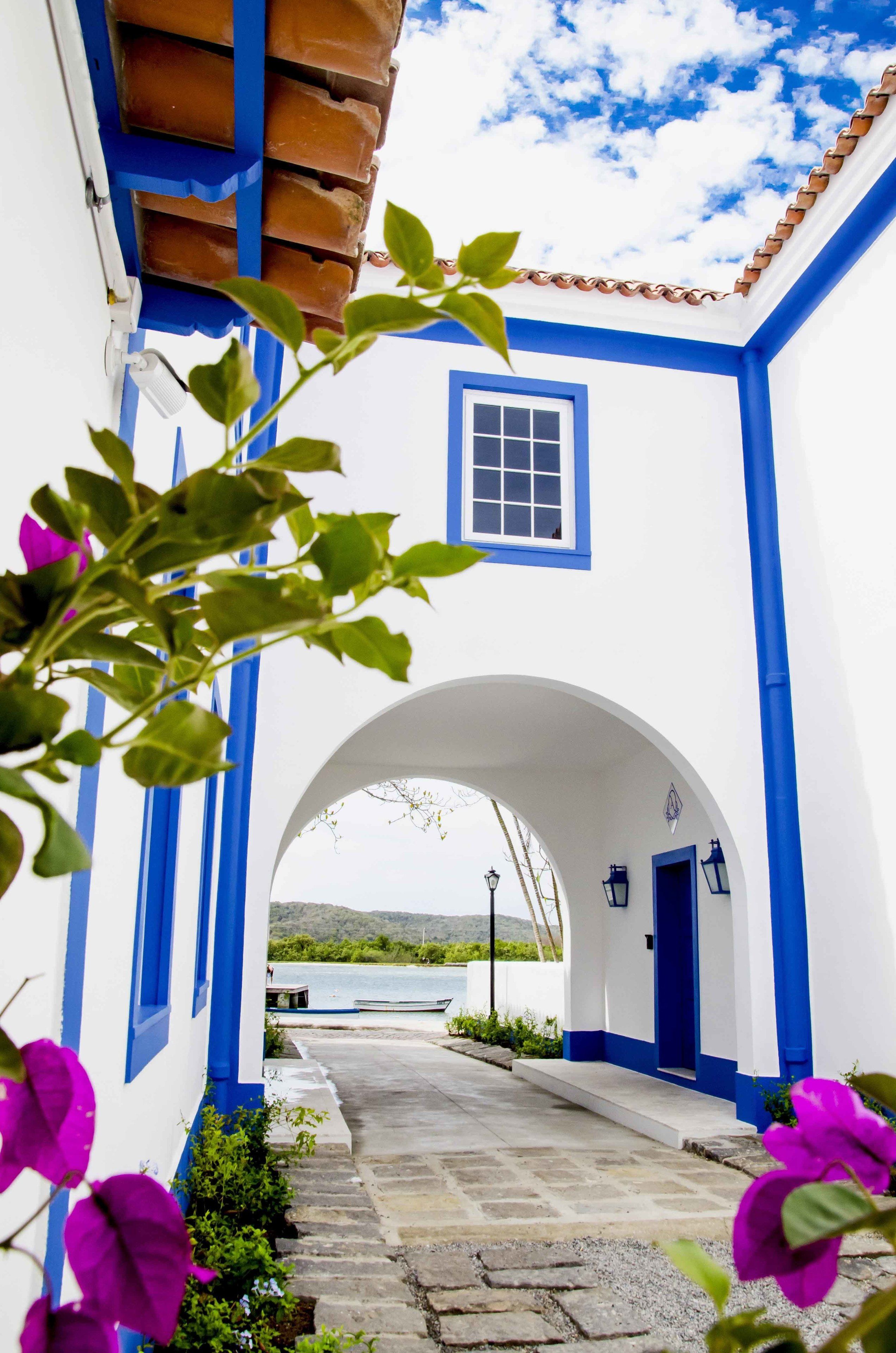 A narrow pathway leading to a white building with blue trim and a tiled roof.