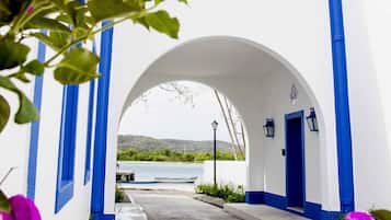 A narrow pathway leading to a white building with blue trim and a tiled roof.