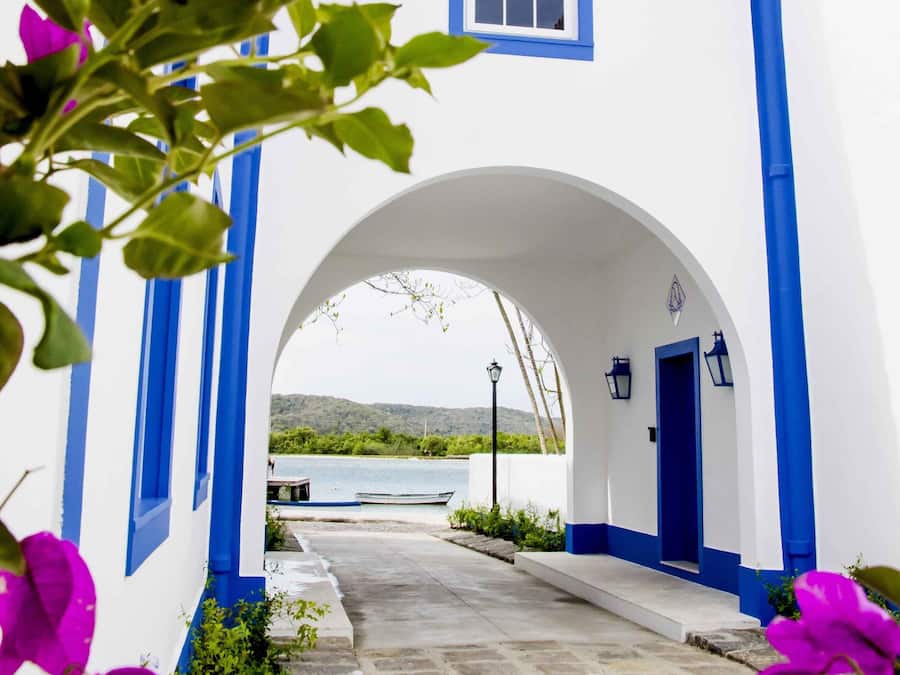 A narrow pathway leading to a white building with blue trim and a tiled roof.