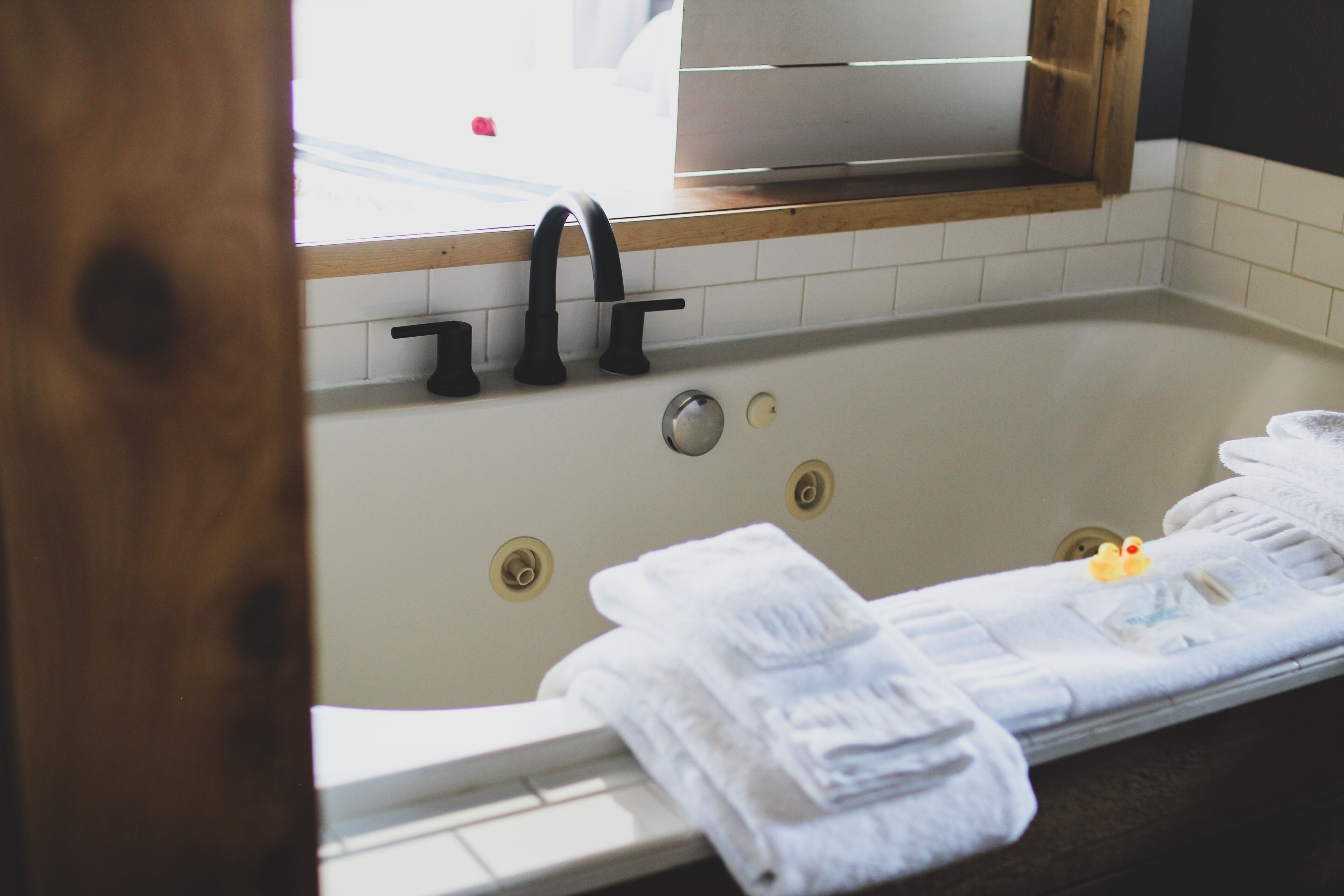Un baño con una bañera, dos grifos y una ventana sobre la bañera.