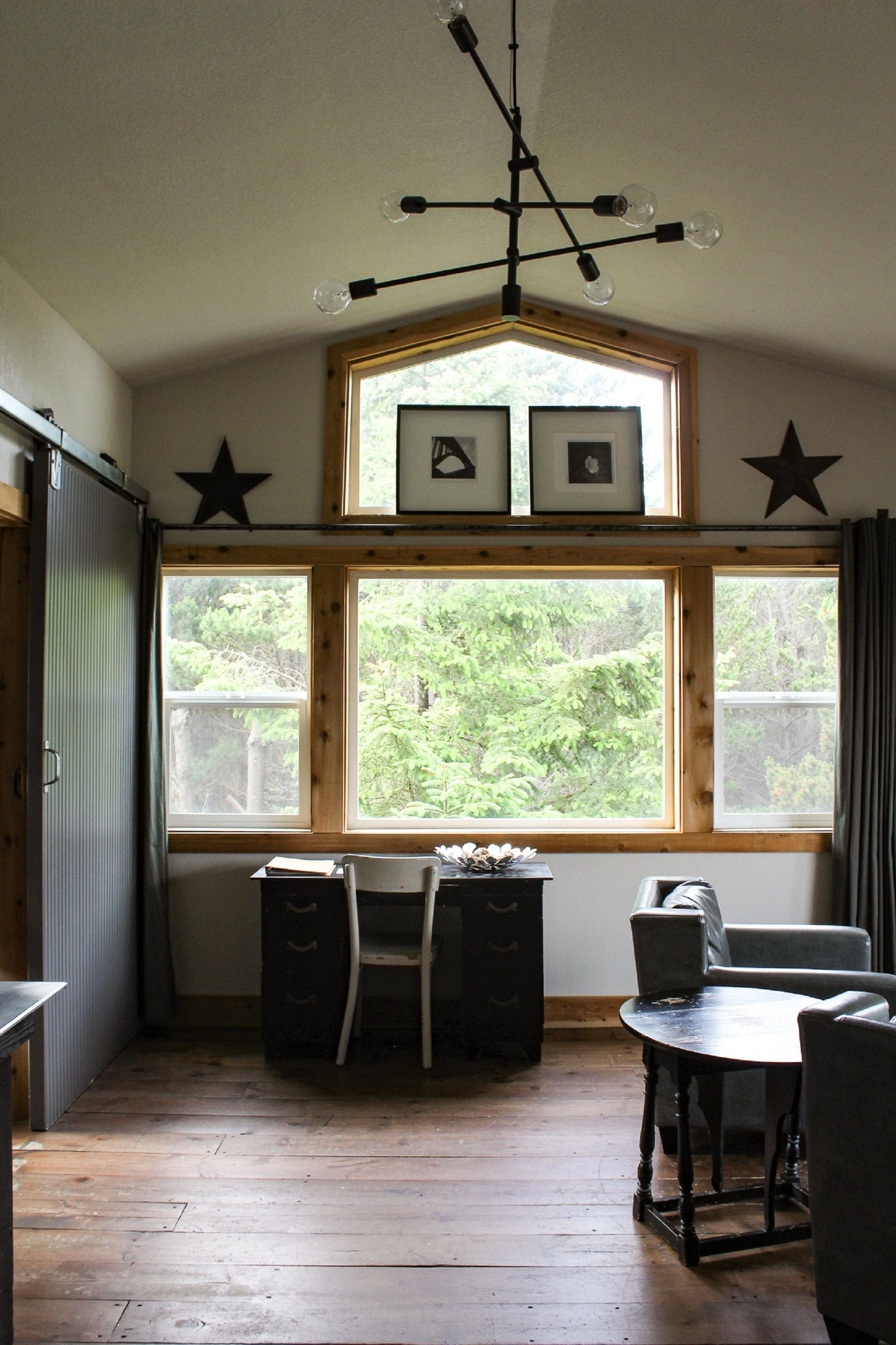 A dining area with a wooden table and chairs, a ceiling light fixture, and a window with a view of greenery.