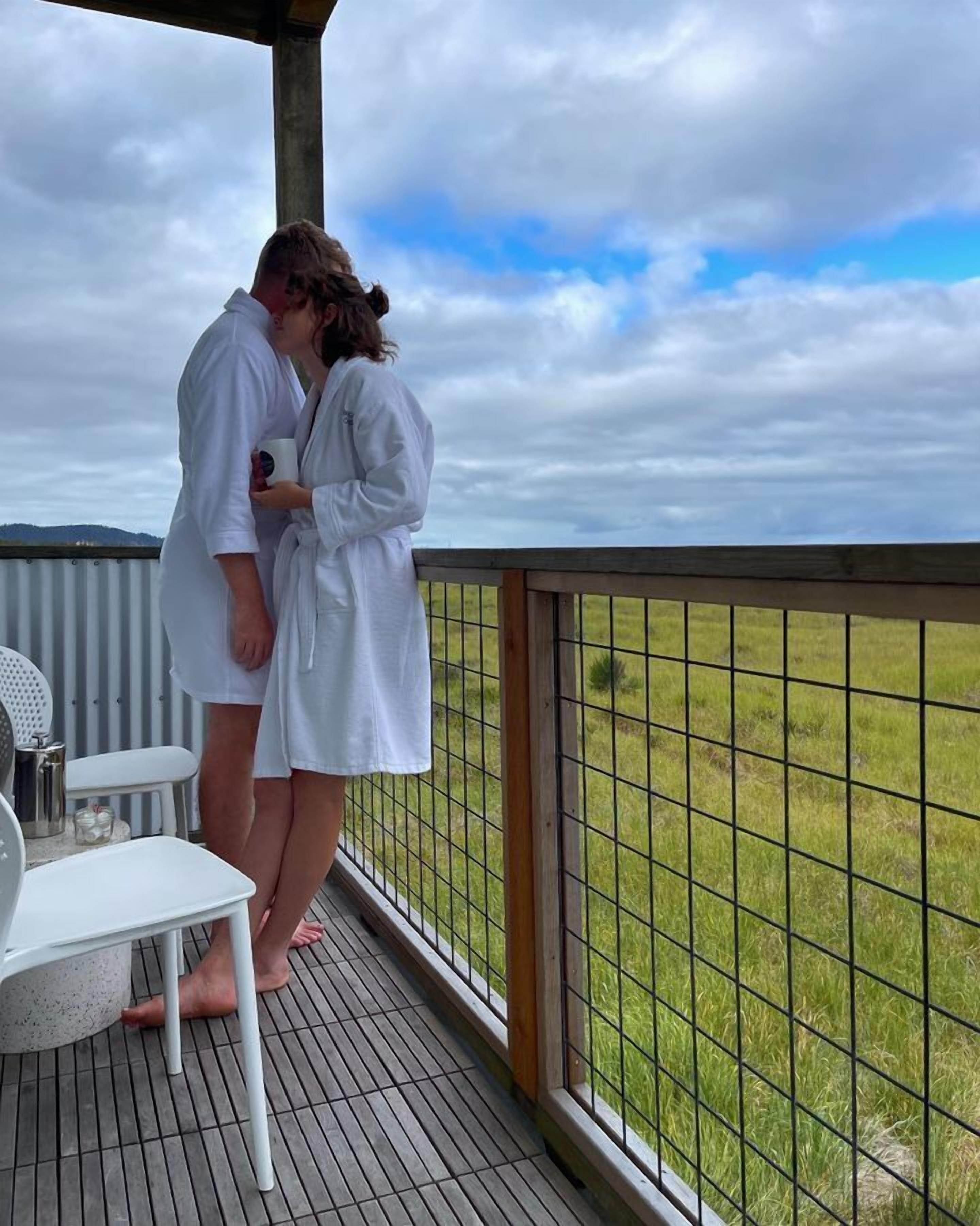 A couple in white robes on a balcony with a view of a grassy field.