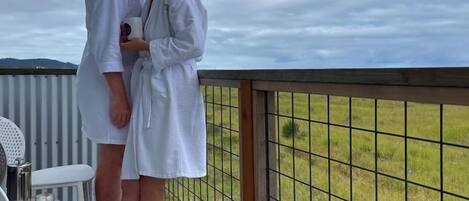 A couple in white robes on a balcony with a view of a grassy field.