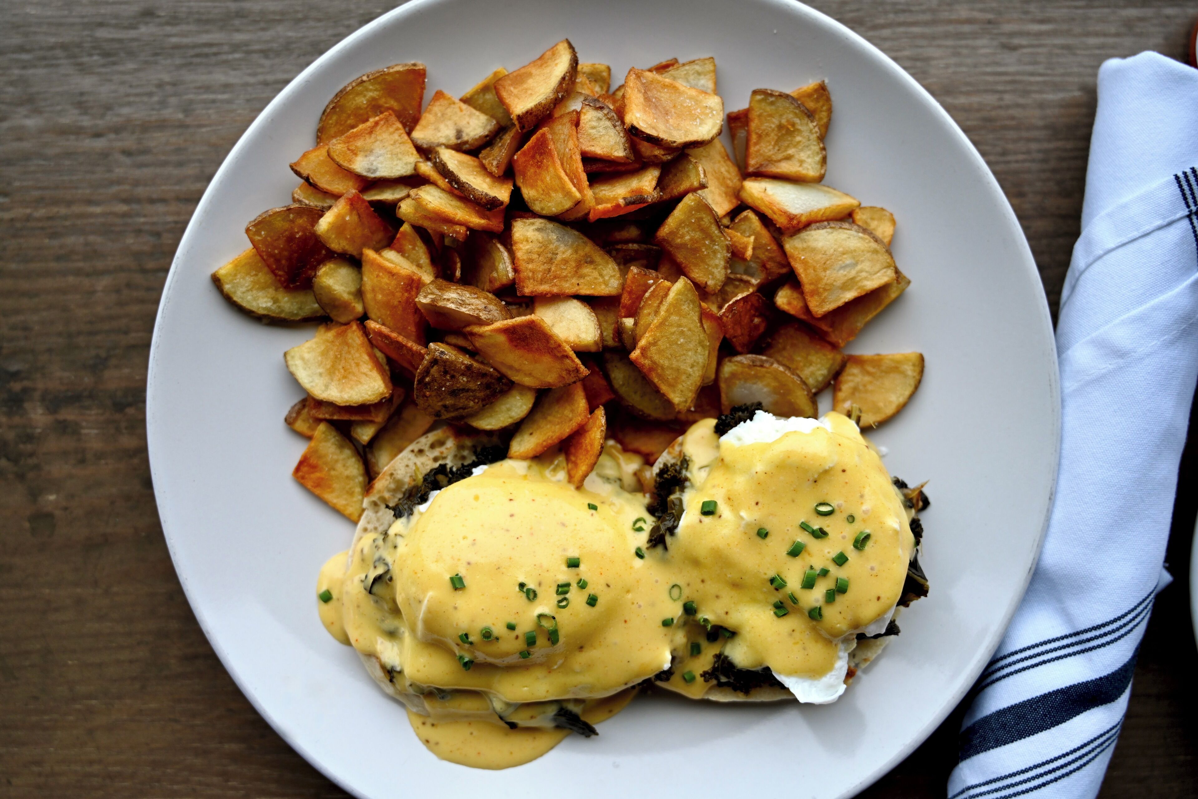 A plate of food with eggs benedict and roasted potatoes.