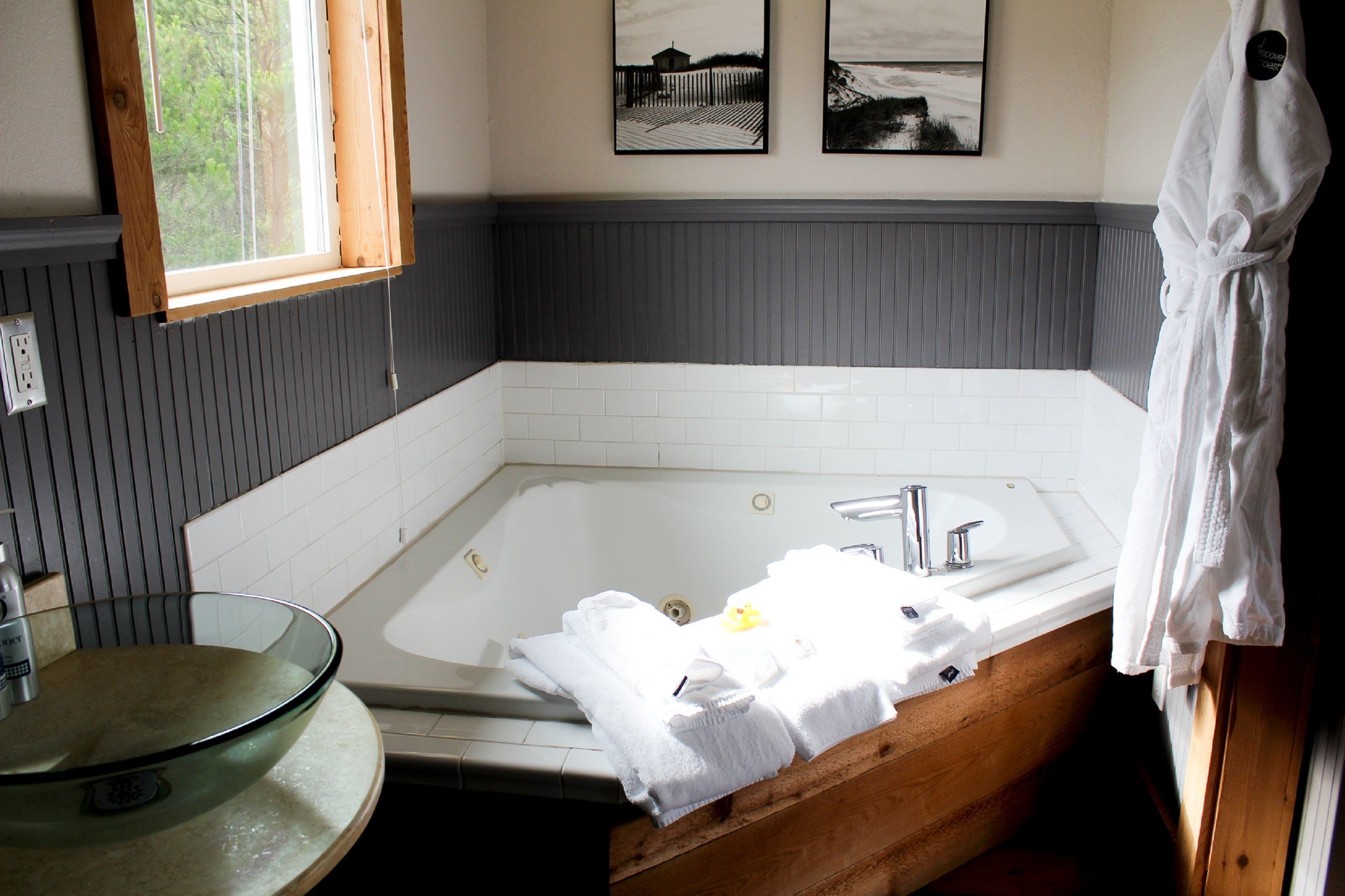 A bathroom with a glass sink, a wooden bathtub, and a window.