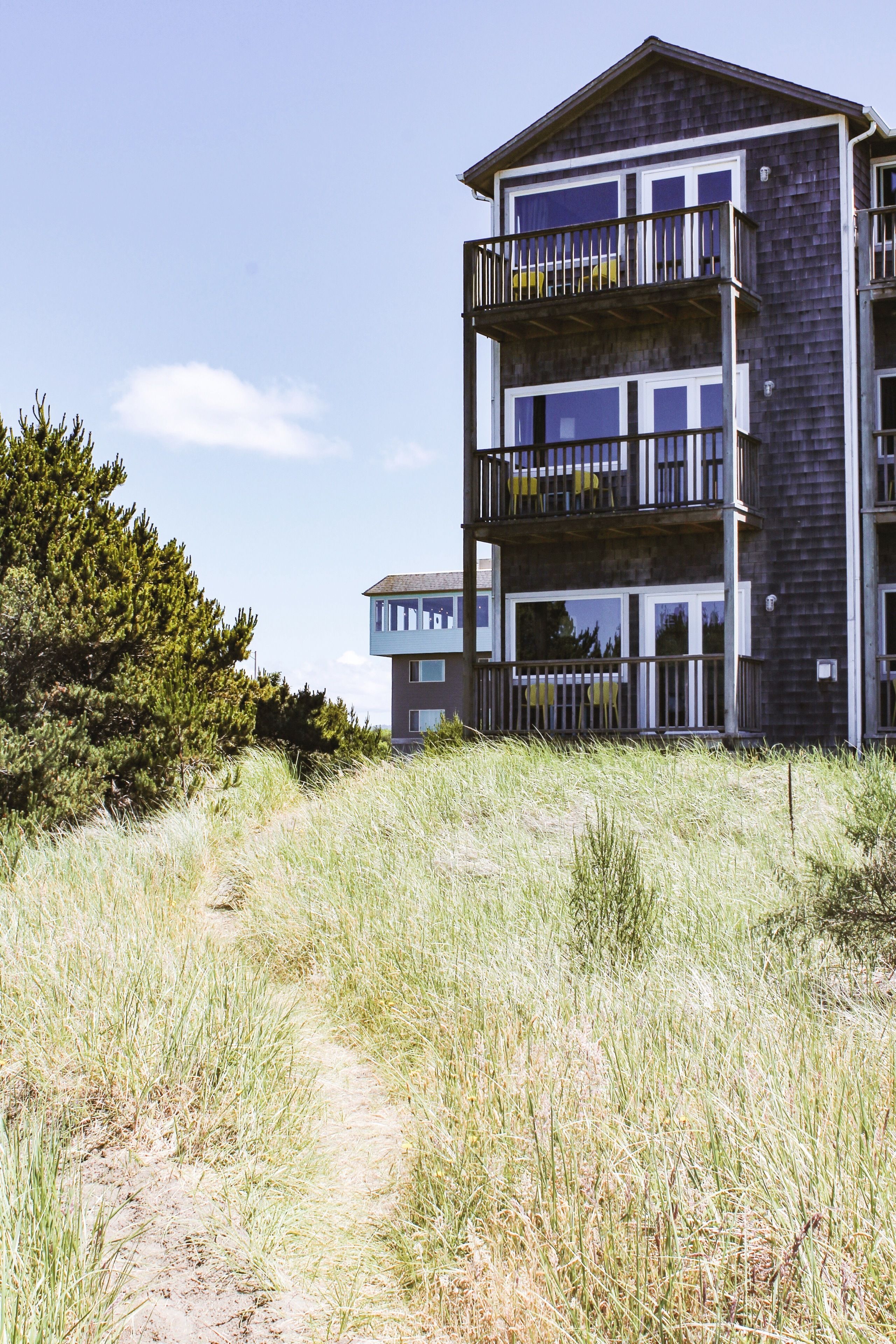 A multi-story building with balconies, situated in a grassy area with trees.