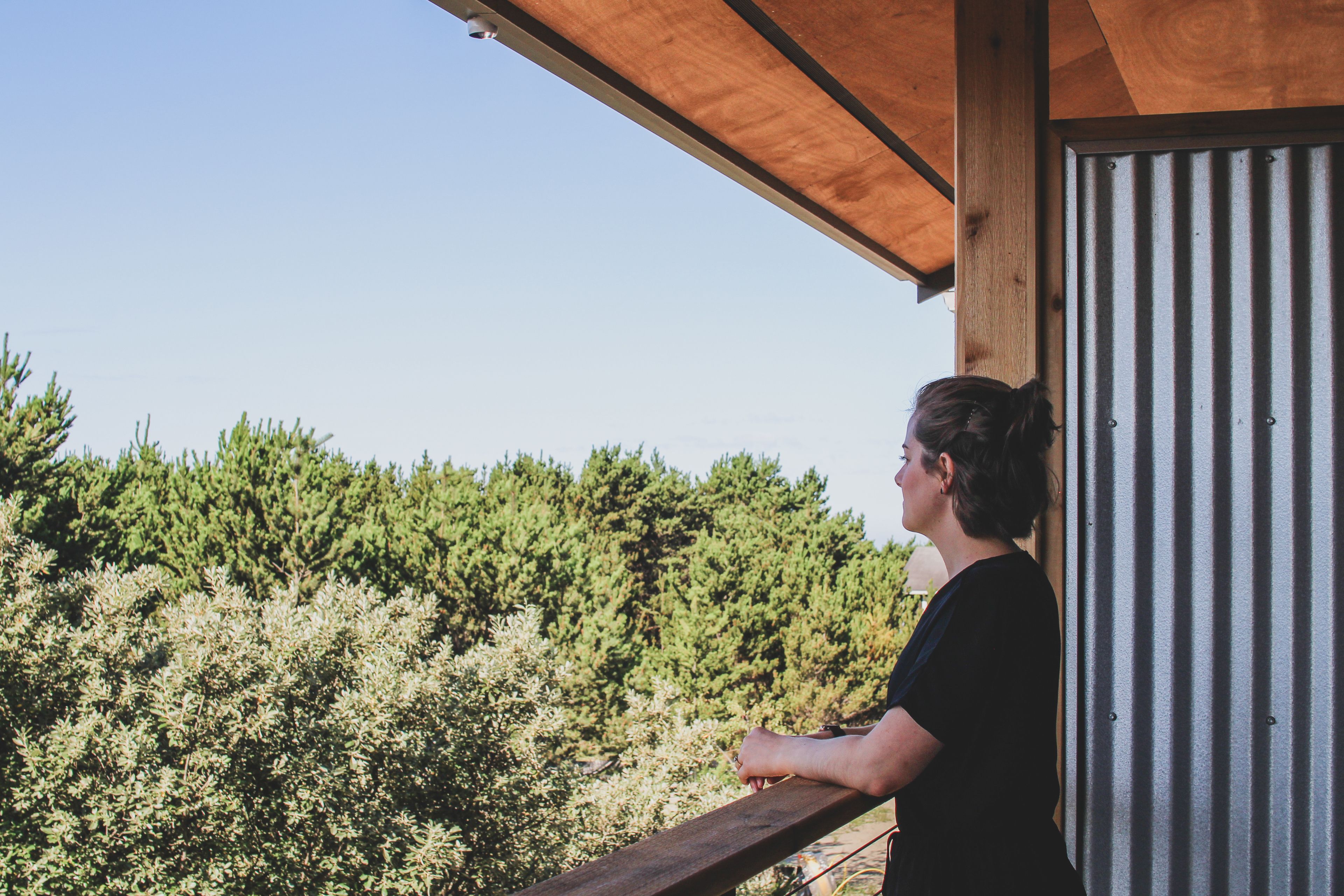 A person standing on a balcony with a view of dense trees.