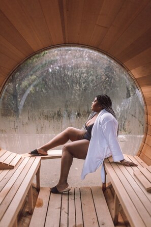 A person sitting on a wooden bench inside a circular wooden structure with a view of trees through a glass dome. - Oceanfront Inn at Discovery Coast (Long Beach)