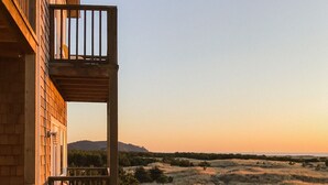 Un edificio de madera con balcón que da a un paisaje herboso y colinas al fondo.