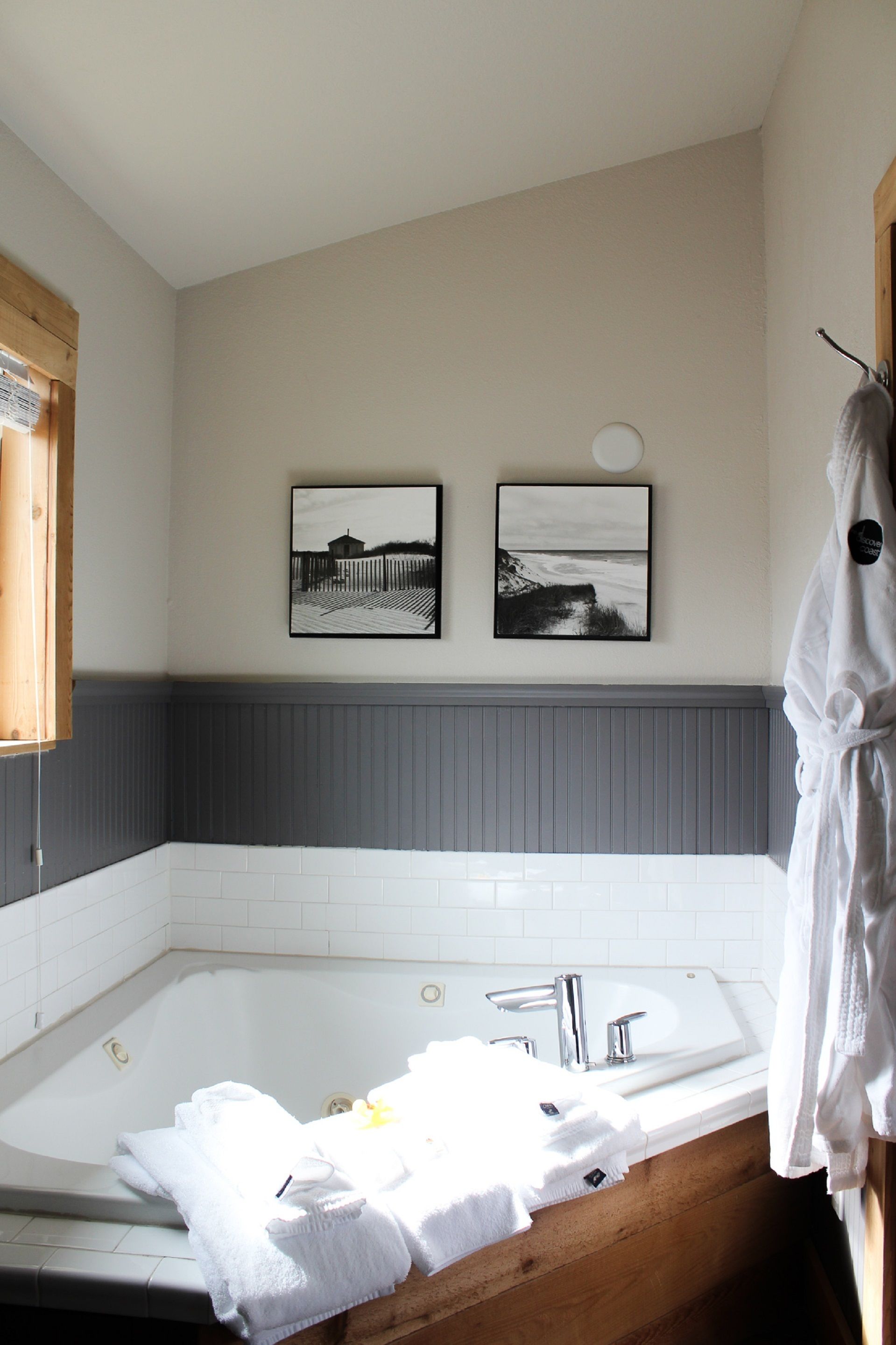 A bathroom with a large bathtub, white tiles, and two framed pictures on the wall.