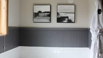 A bathroom with a large bathtub, white tiles, and two framed pictures on the wall.