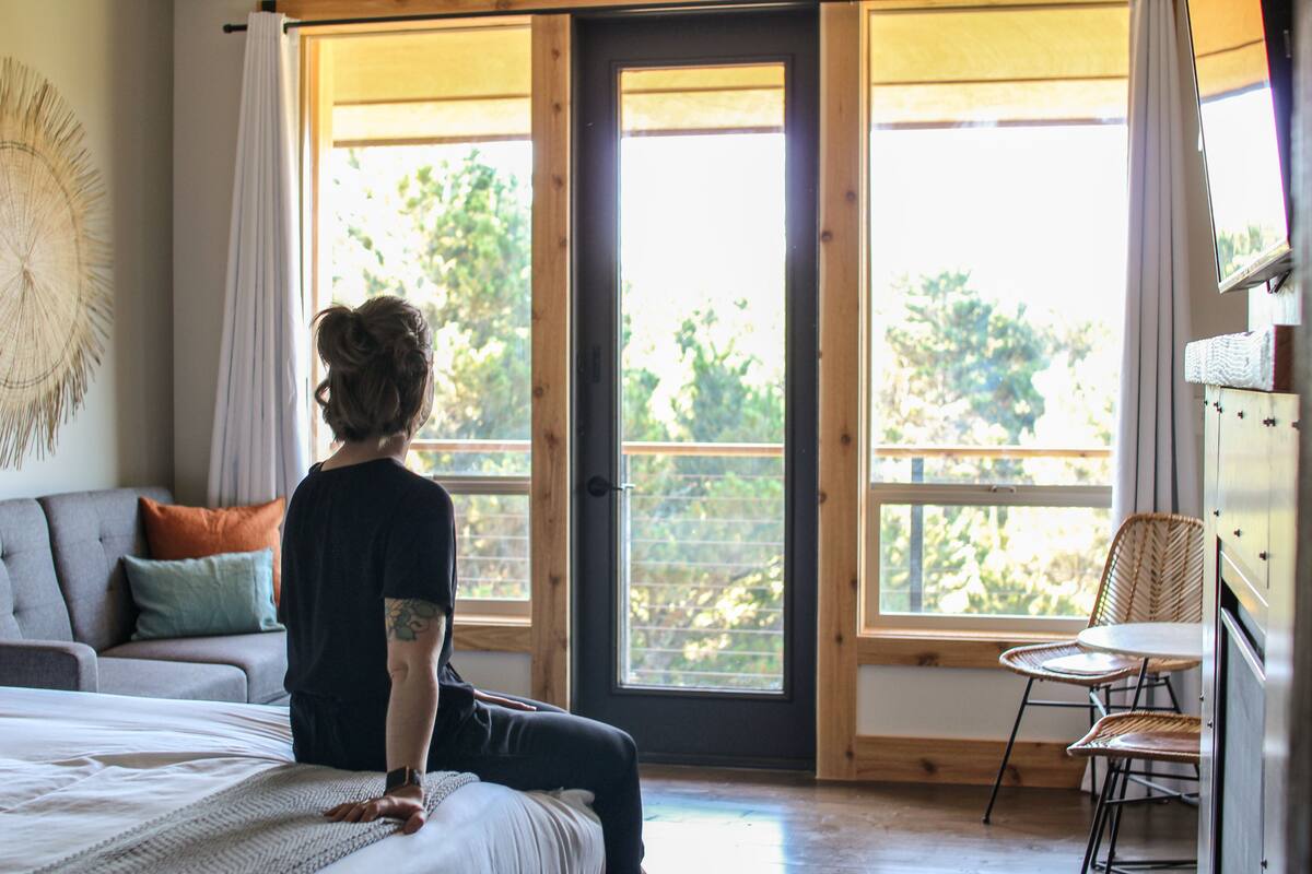 Quarto com cama, sofá e poltrona. Janelas amplas com vista para árvores.