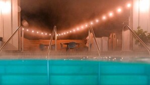 Una piscina con escalones de acceso, rodeada de una terraza de madera y mobiliario exterior.