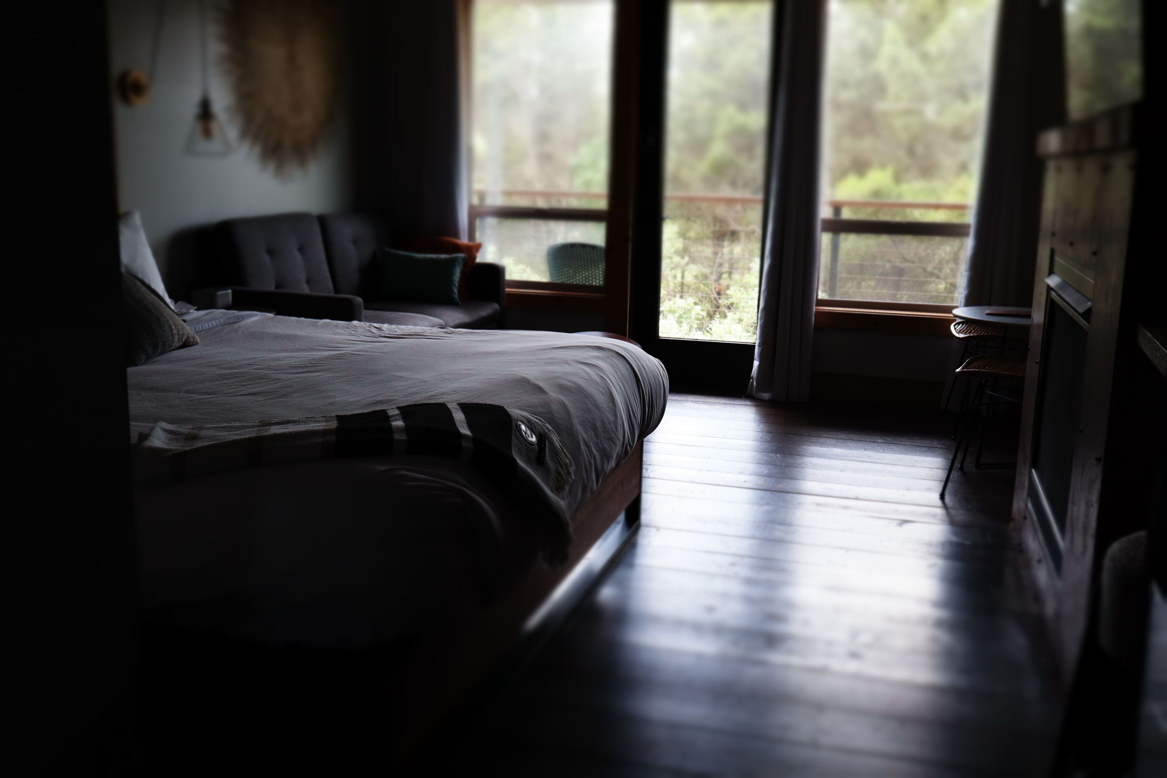A dimly lit room with a large bed and a window overlooking a forested area.