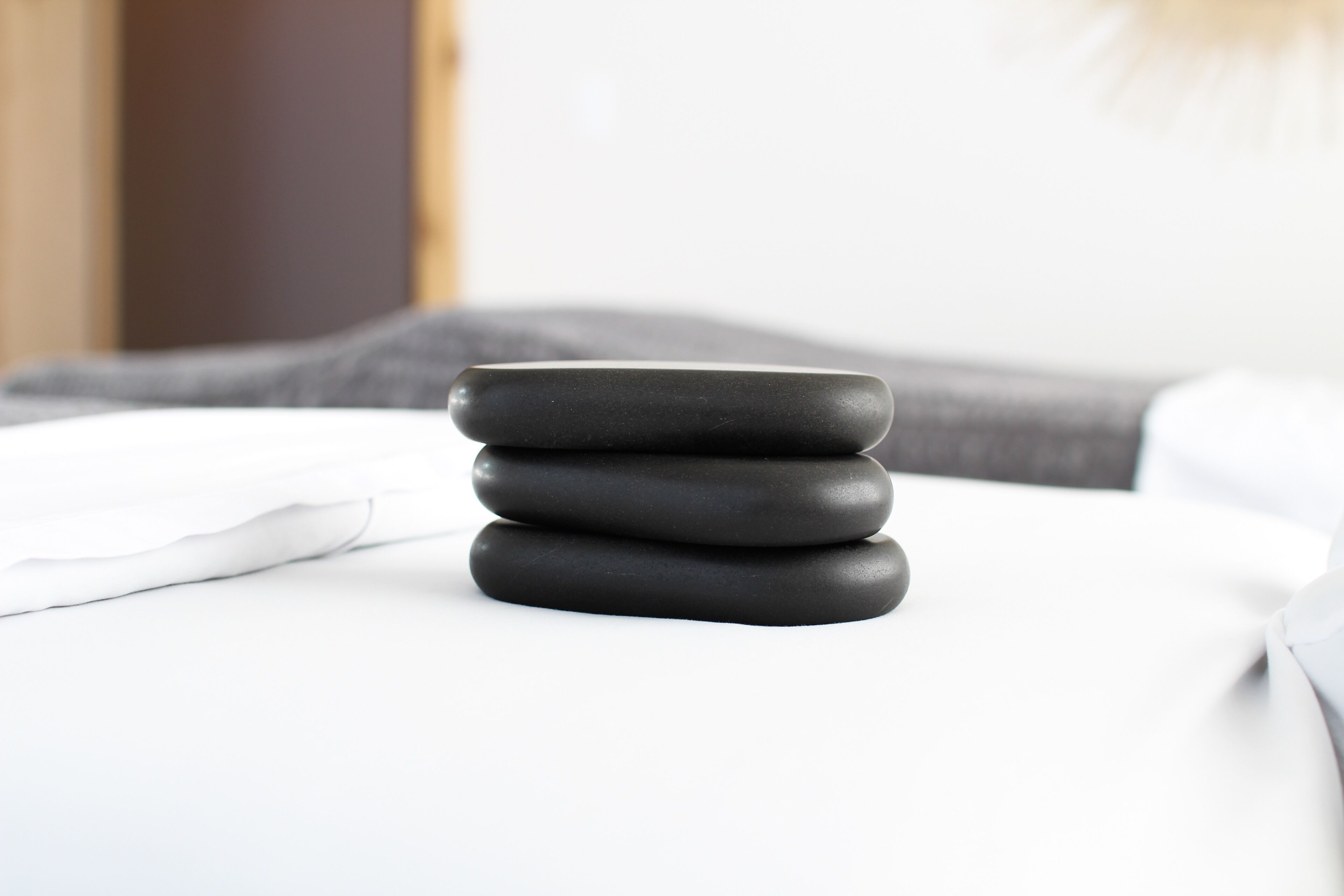 A stack of black stones on a white bed with a gray pillow in the background.