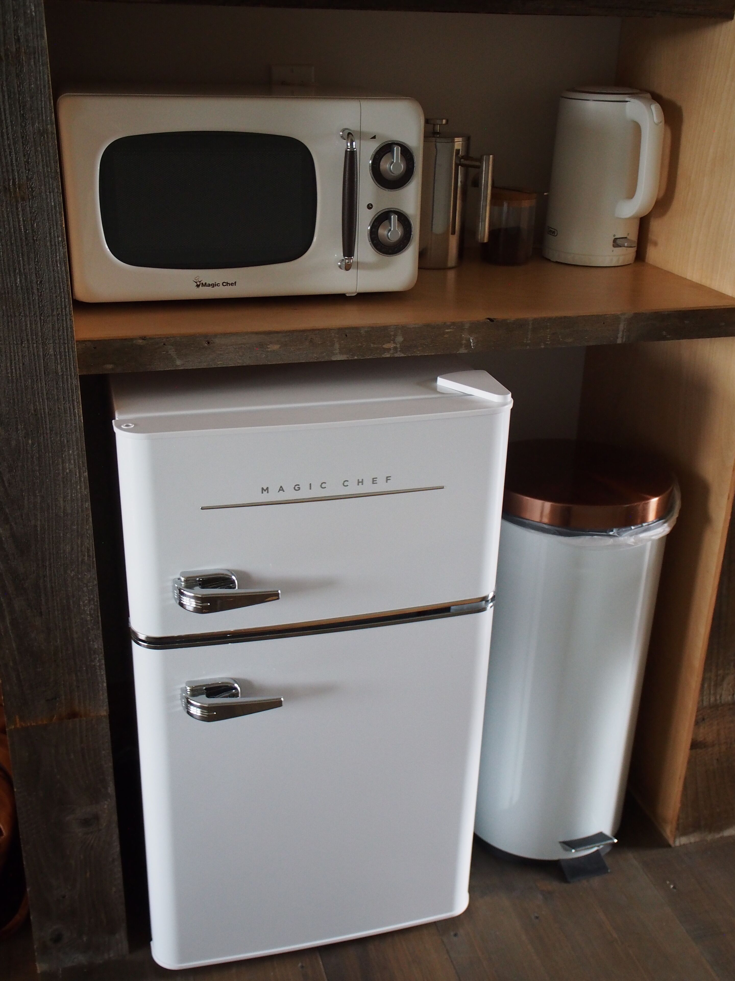 A compact kitchenette with a microwave, a small refrigerator, and a trash bin.