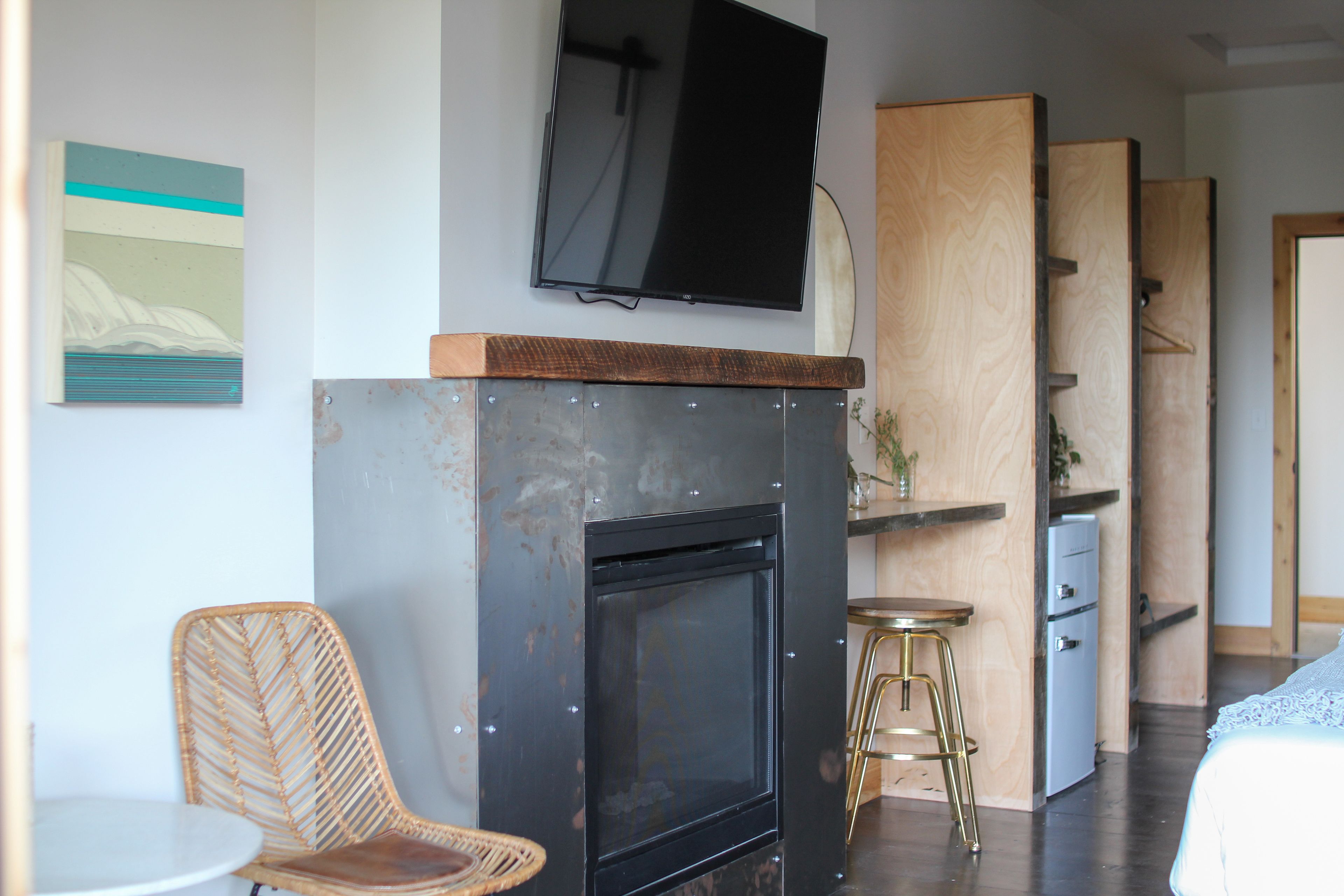 A modern room with a fireplace, a television mounted above it, a wicker chair, a small round table, and a wooden cabinet.