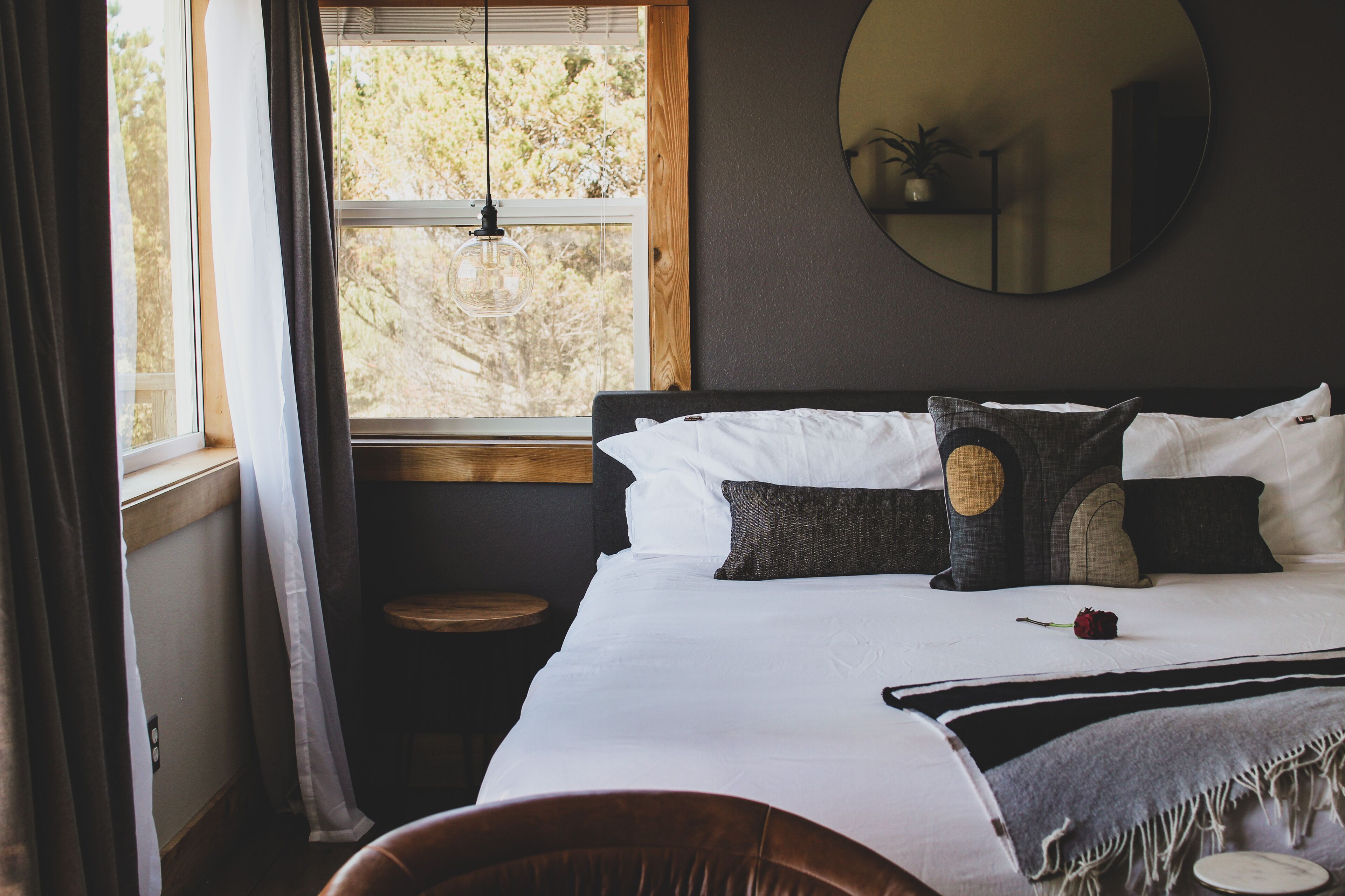 Une chambre avec un grand lit, un miroir rond, une petite table et une fenêtre avec des rideaux.