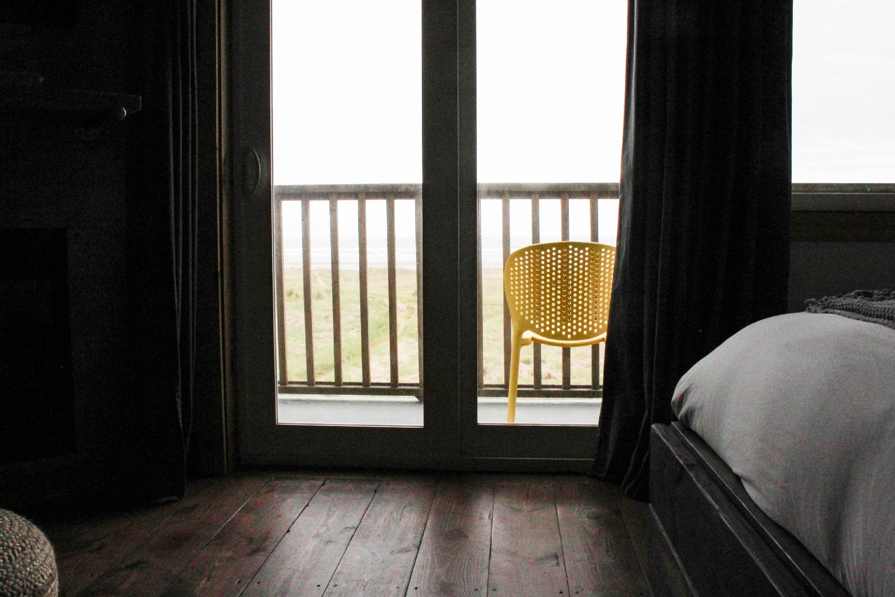 Une chambre avec un lit, un plancher en bois, une fenêtre donnant sur la plage et une chaise à l’extérieur.