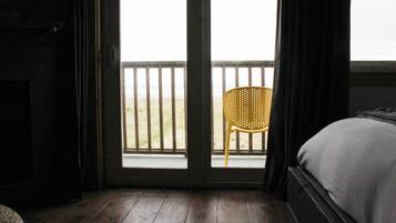 Une chambre avec un lit, un plancher en bois, une fenêtre donnant sur la plage et une chaise à l’extérieur.