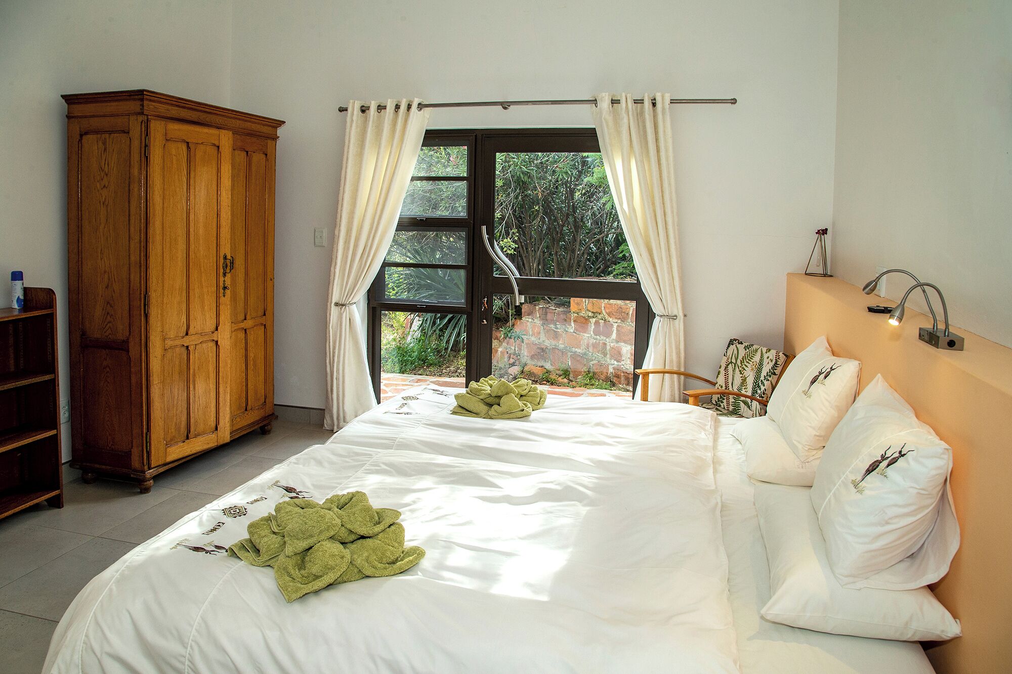 Ein Schlafzimmer mit einem großen Bett, einem Holzschrank und Blick ins Grüne durch ein Fenster.
