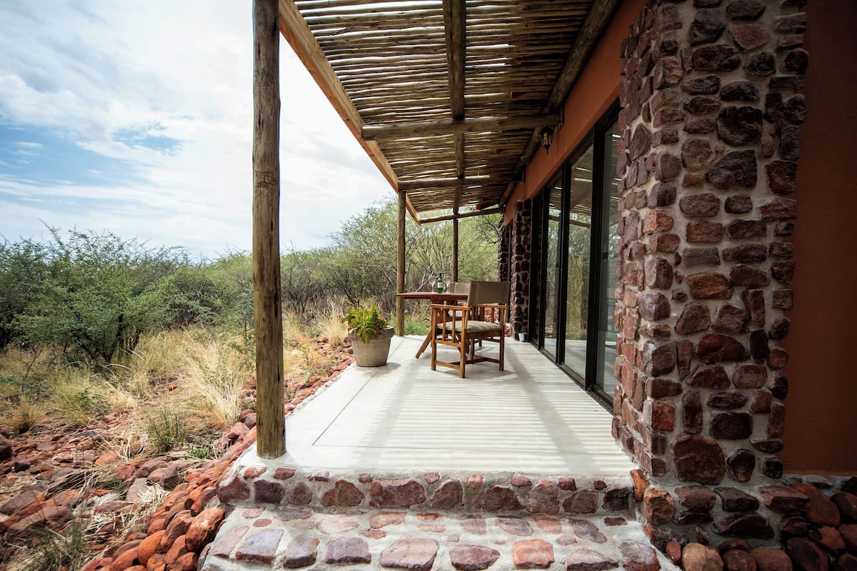 A covered outdoor patio with a stone wall, a table with chairs, and a potted plant.