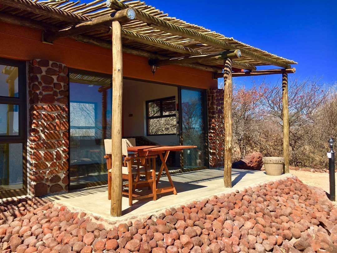 A covered patio area with a stone wall, wooden furniture, and a clear view of the surrounding landscape.