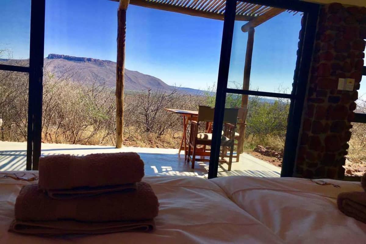 A bed with a view of a mountainous landscape through large windows.