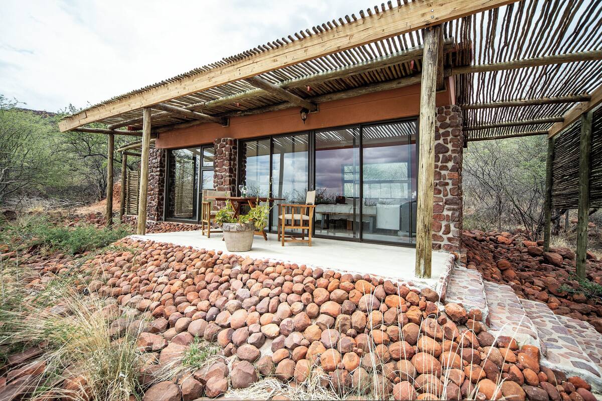 A modern building with a stone facade, large windows, and a covered patio area with a stone pathway.