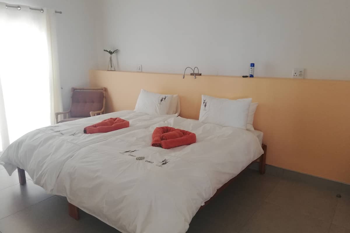 A hotel room with a bed, two pillows, a nightstand, a chair, and a wall-mounted shelf.