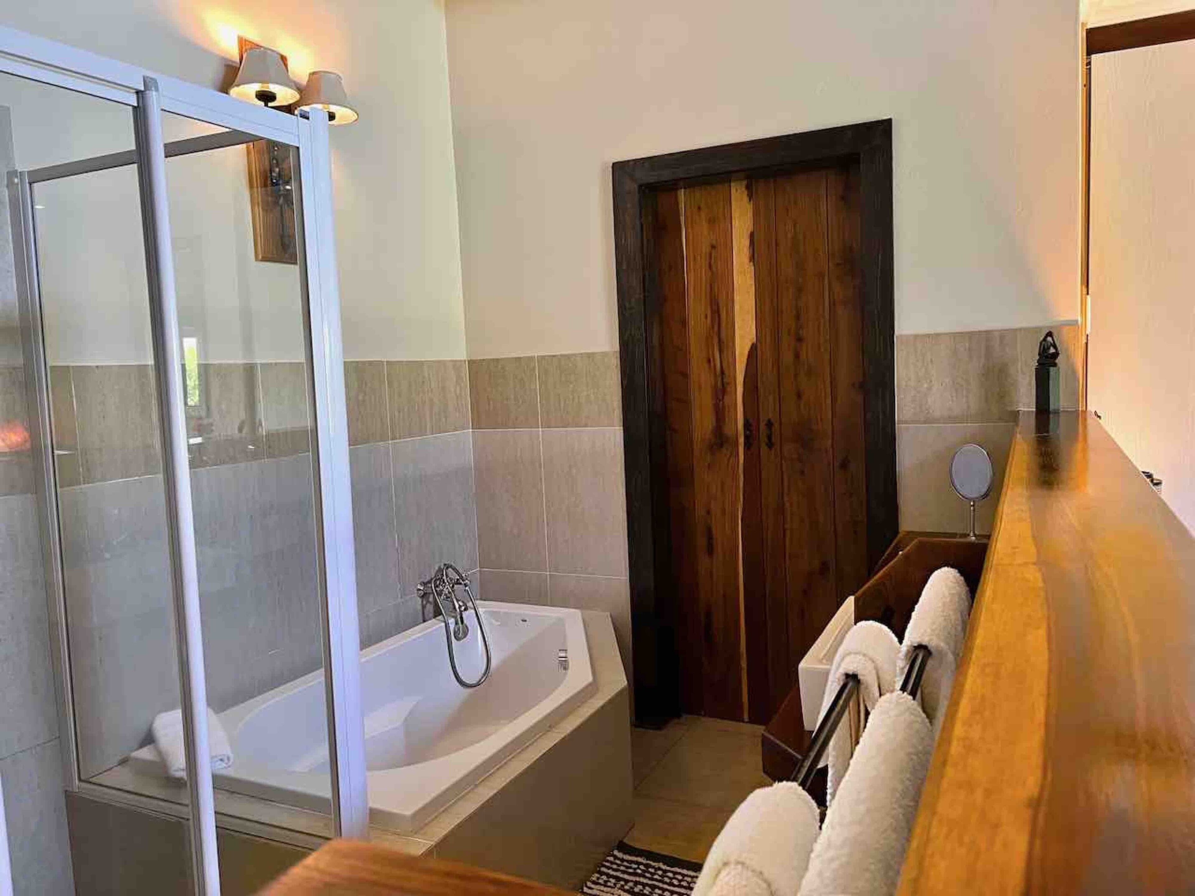 Une salle de bain avec une douche à parois de verre, une porte en bois et une baignoire blanche.