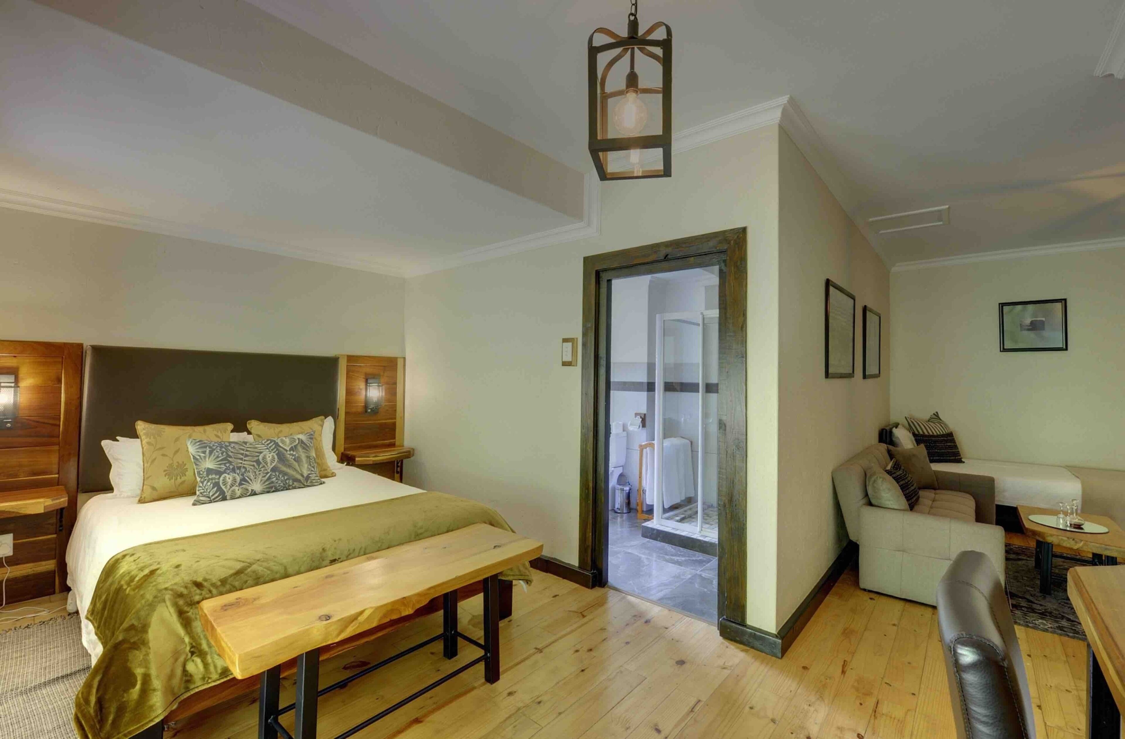 Un dormitorio con cama, banco, cabecera de madera y un acceso a una sala de estar con sofá y mesa.