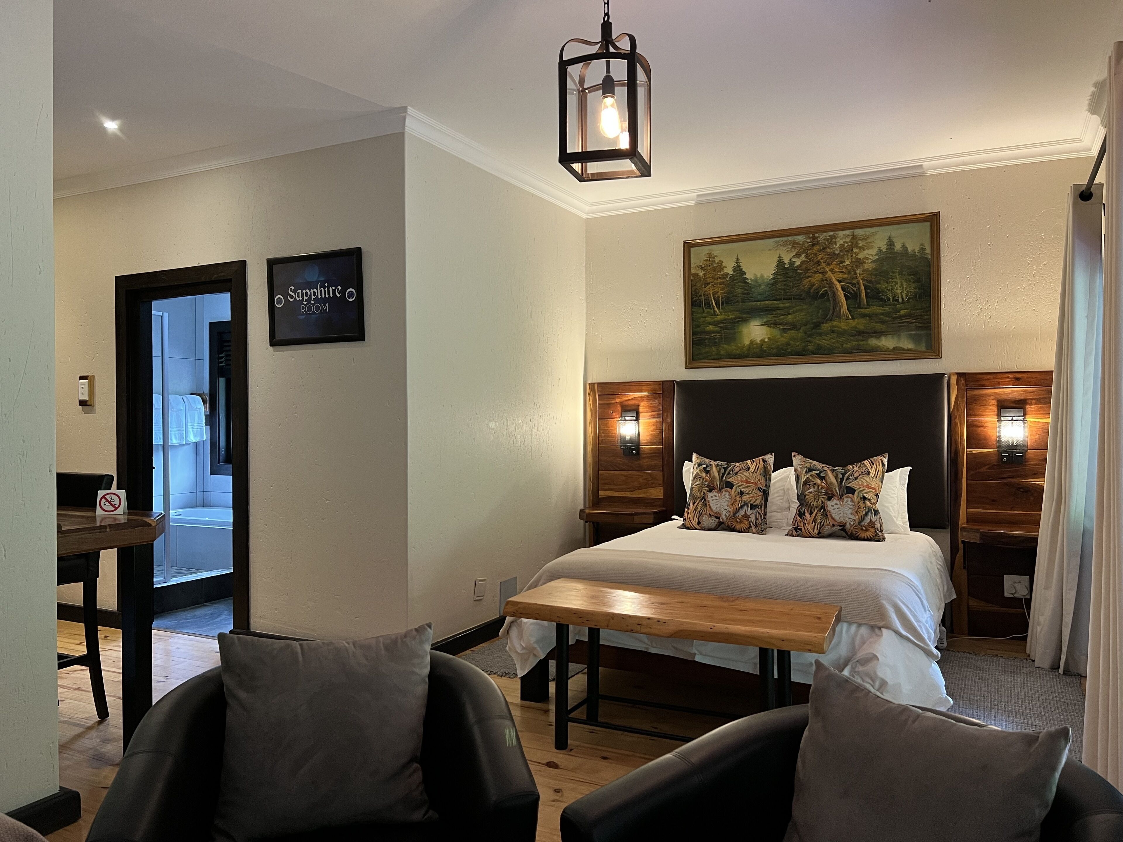 A hotel room with a bed, two nightstands with lamps, a bench, and a painting on the wall.