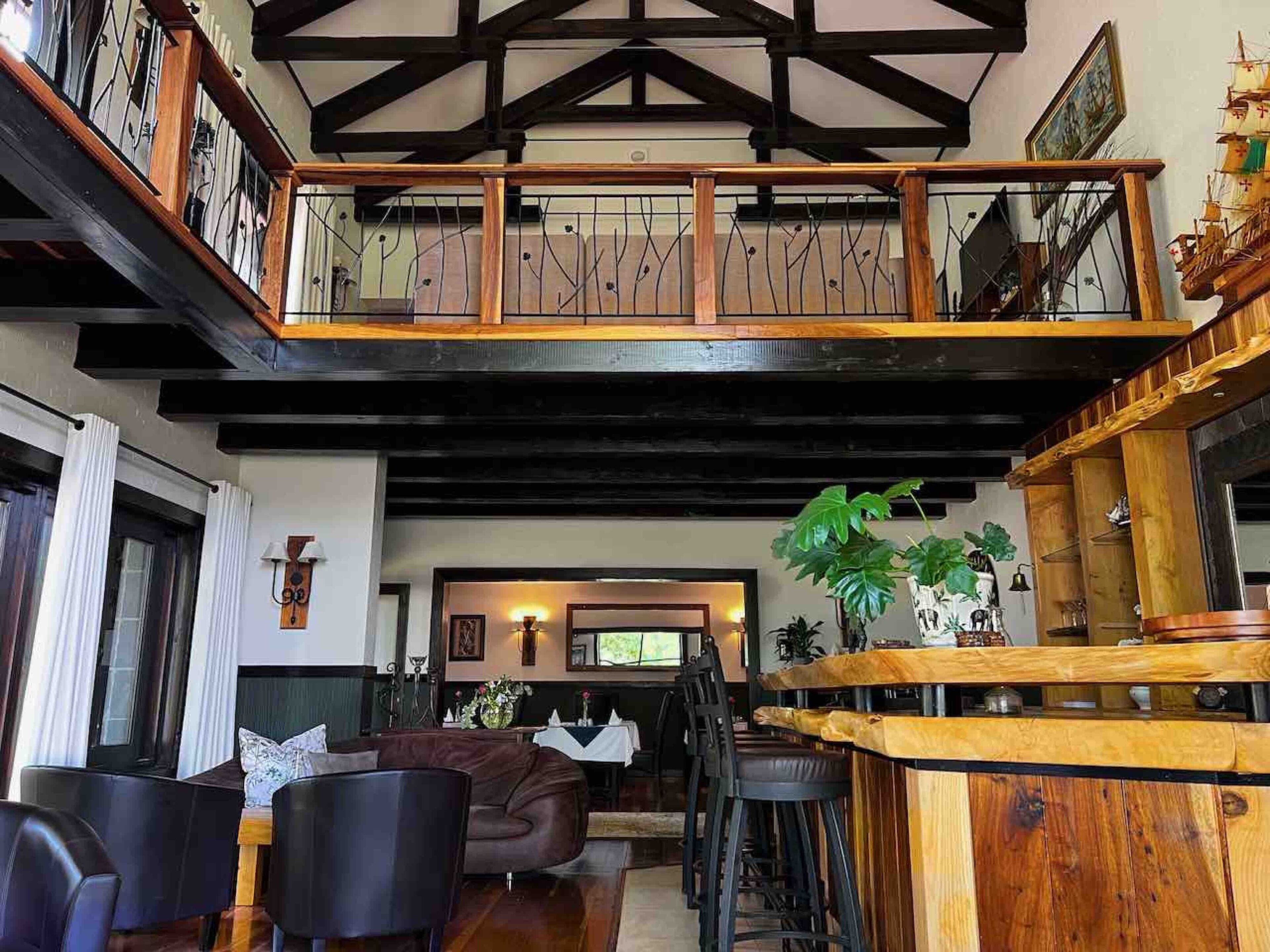 A spacious loft-style living area with a high ceiling, exposed beams, and a mezzanine level with a balcony.