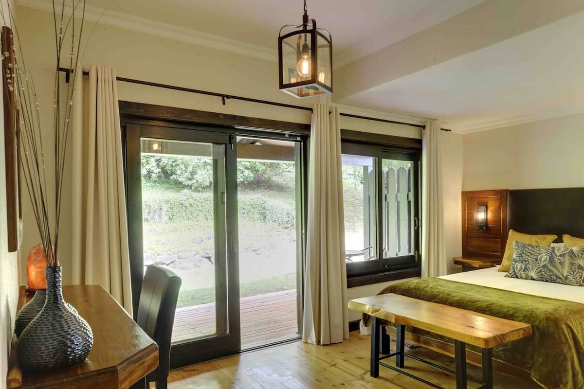 Un dormitorio con cama, un banco, una mesa, un jarrón y vistas al exterior.