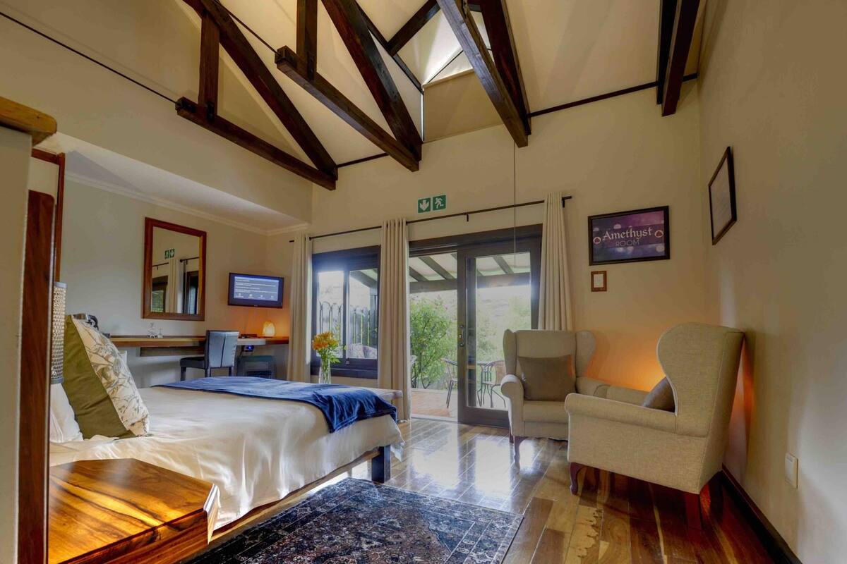 Habitación de hotel con cama, escritorio con computadora, silla y balcón con cortinas.