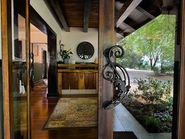 Uma área de recepção com um banco de madeira, um relógio de parede grande e vista para um jardim através de uma porta aberta.