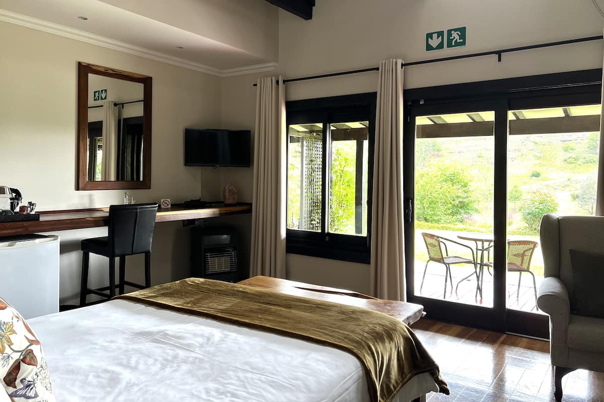 Una habitación de hotel con cama, escritorio, silla, televisión y balcón con sillas.