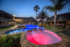 A pool with a unique color gradient, surrounded by stone tiles and palm trees.